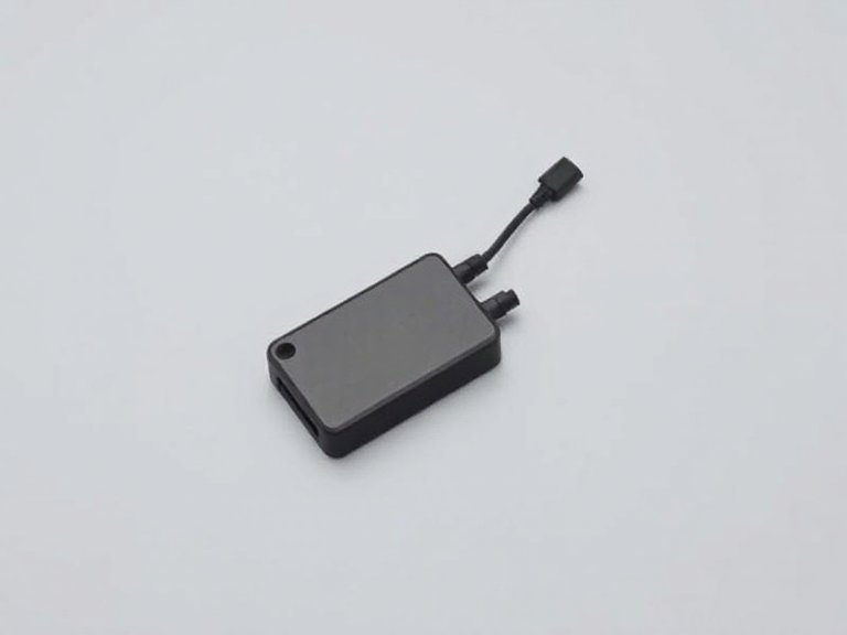 Módulo electrónico negro con su cable de conexión sobre una superficie gris