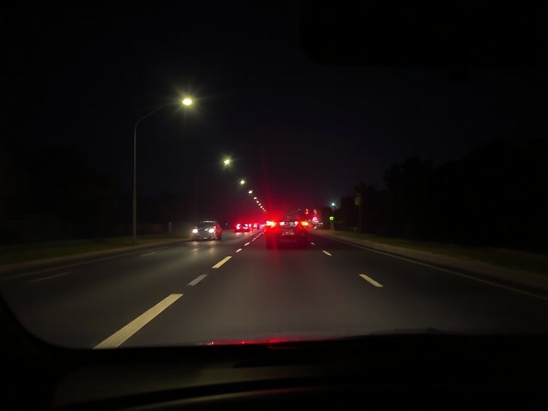 Carretera de noche con un turismo cerca por delante mostrando las luces traseras