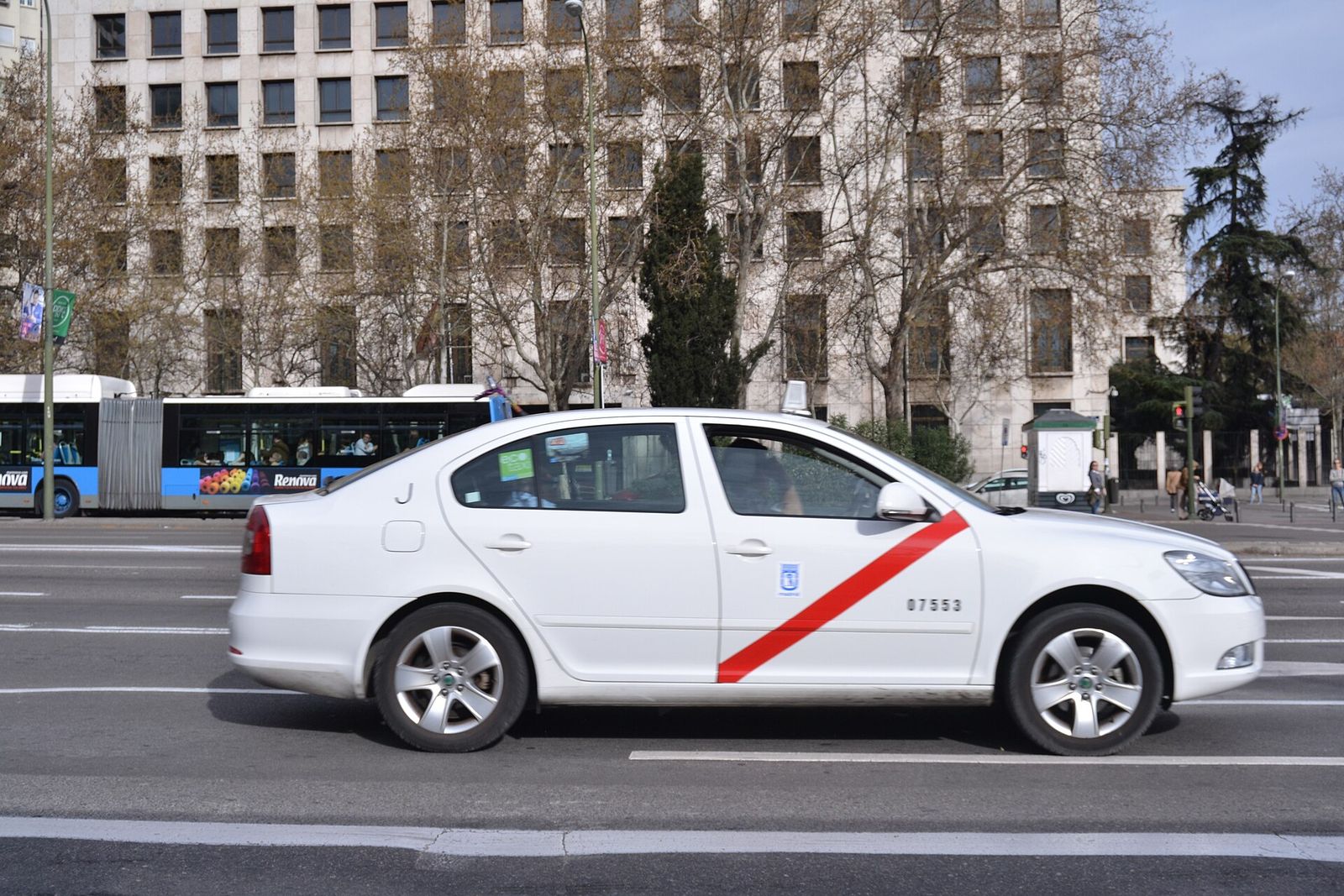 Taxi blanco con banda roja circulando por una avenida de Madrid