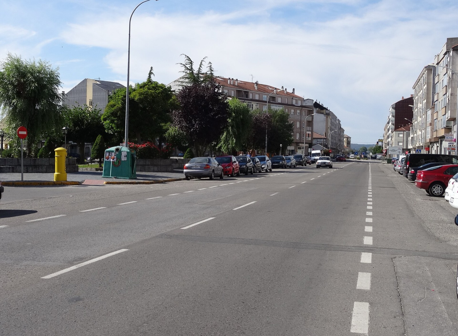 Carretera que atraviesa una población, con edificios y coches aparcados a ambos lados